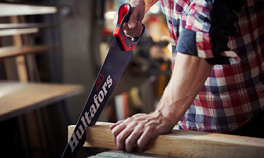 Snekker i rød-hvit rutete skjorte sager lyst tre med svart/rødt Hultafors-sag i verksted