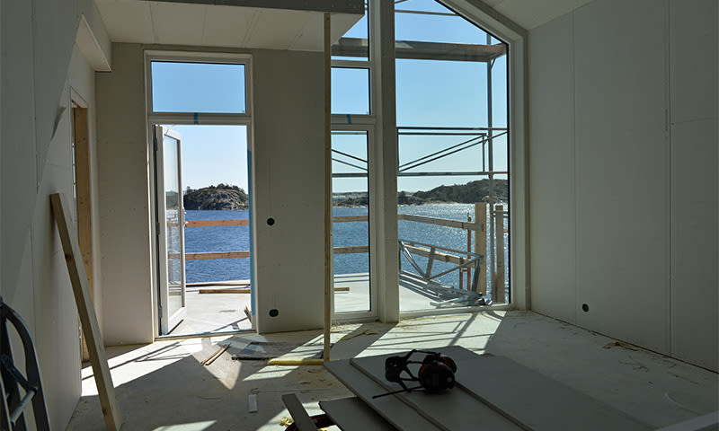Uferdig rom med lysåpning, byggematerialer og glassdør mot blått hav og øyer