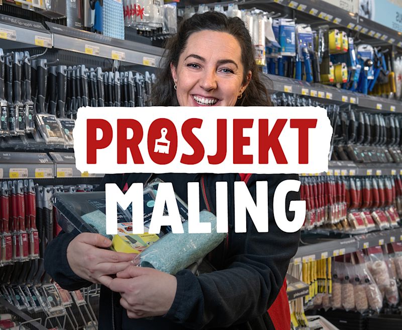 Smilende butikkmedarbeider holder maleutstyr i en jernvarebutikk med teksten "PROSJEKT MALING" i forgrunnen.