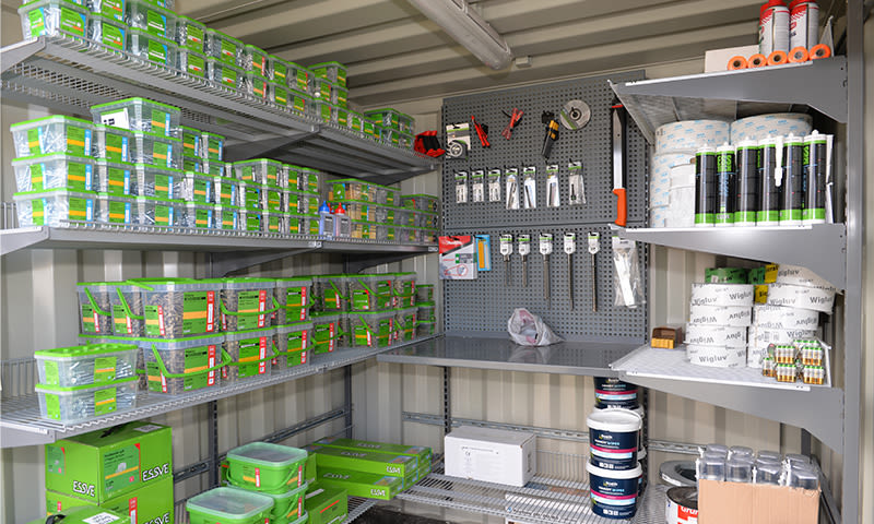 Metallhylle med grønne ESSE-skruebokser, verktøy hengende på perforert bakvegg og hvite tetningsrør