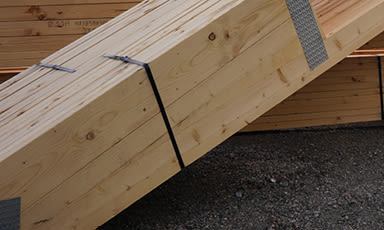 Lyse treplanker stablet på grus på byggeplass, bundet med svart stropp.