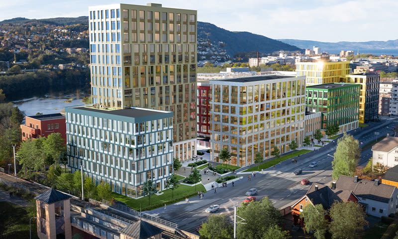 Moderne fleretasjers fargerike kontorbygg ved vei og elv, omgitt av trær og åser i bakgrunnen.