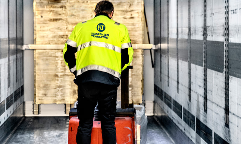 Mann i neongul Kristensen Transport-jakke skyver pall inn i lastebilhenger.