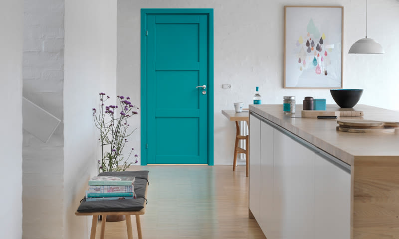 Åpent kjøkken med trebenk, turkis dør, grå benk og lilla blomster