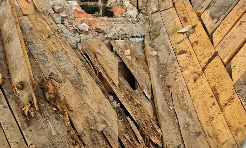 Råtne, ujevne gulvbord av grått og brunt tre med synlig mur under