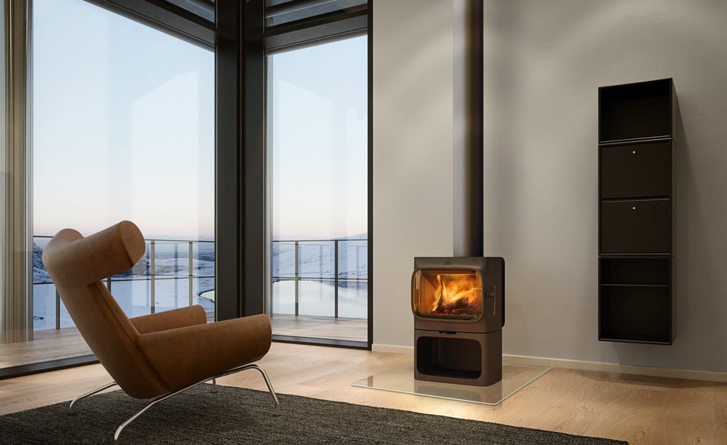 Moderne stue med brun lenestol, svart peisovn med flammer og glassvegg mot snødekt fjord