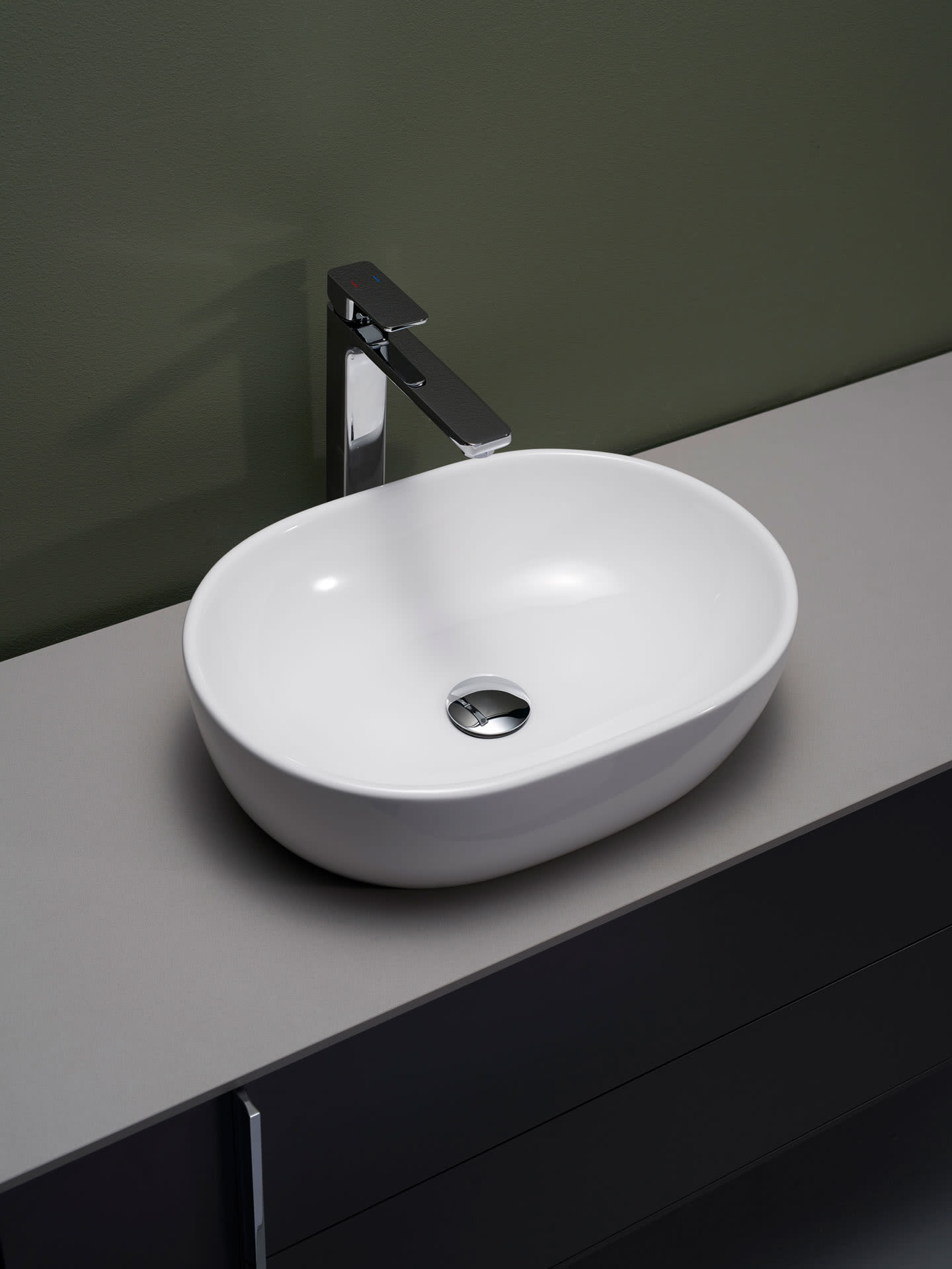 Hvit oval servantskål på grå benkeplate med krom armatur mot olivengrønn vegg.