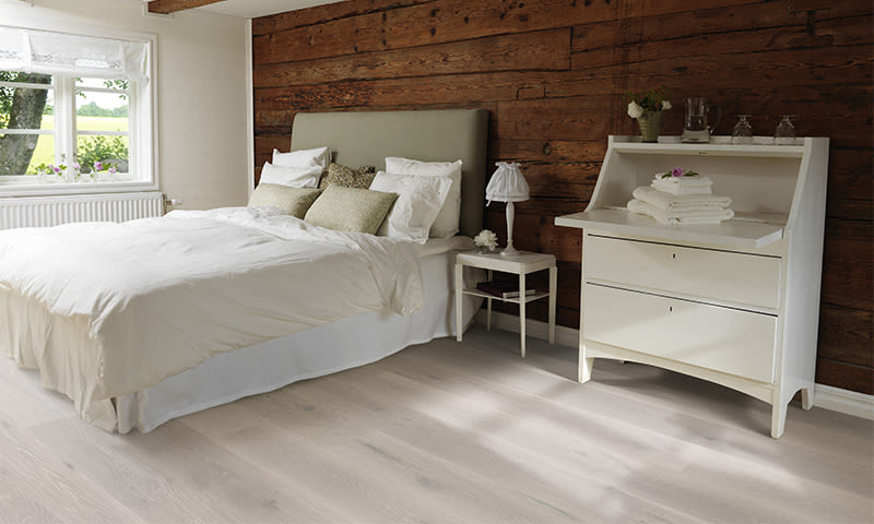 Lyst soverom med hvit seng, grønn ryggpute, trevegg og hvit kommode ved vindu.