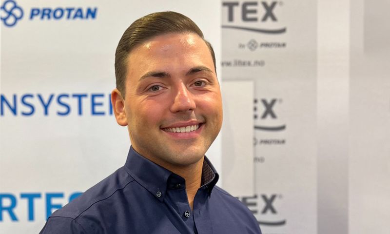 Mann i mørk blå skjorte foran hvit messevegg med blå Protan- og Tex-logoer