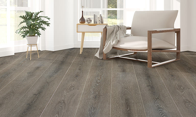 Lyst rom med grått tregulv, hvit lenestol i tre, sidebord m/bøker og vase, grønn plante.