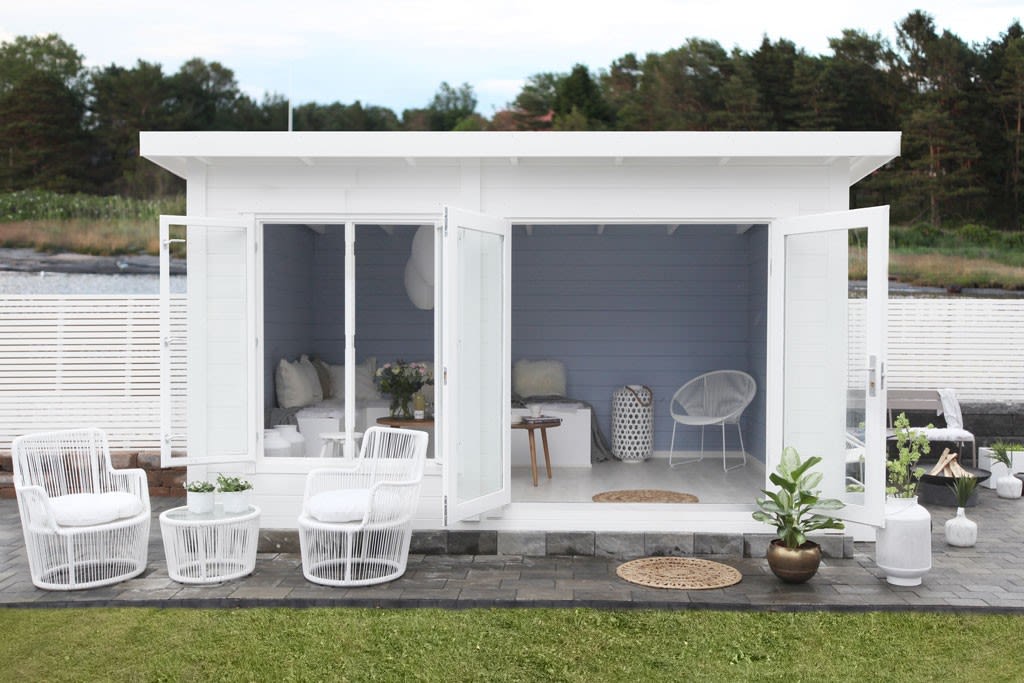 Hvit hagehytte med åpne doble dører, lyseblå vegger, hvite rottingstoler og planter