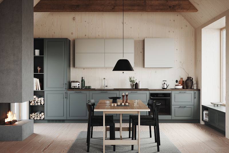 Lyst trekjøkken med grønnblå skap, svart pendellampe, trebord med svarte stoler og peis.