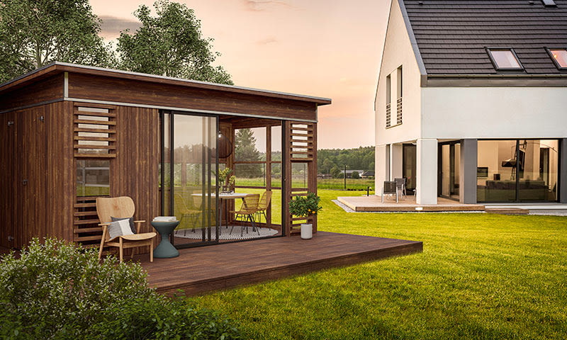 Moderne hvitt hus med trepaviljong, sitteplass på terrasse og grønn gressplen i solnedgang.