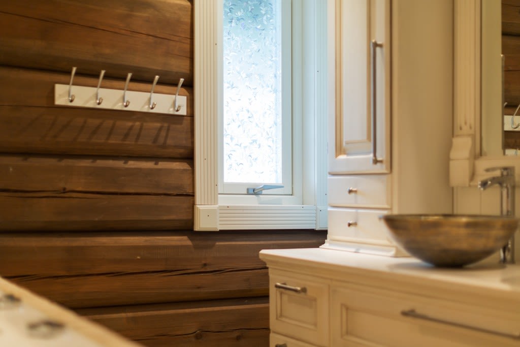 Bad med mørke trepaneler, hvit innredning, frostet vindu og rund metallskålvask.