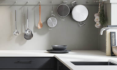 Moderne grått kjøkkenhjørne med hvit benkeplate, hengende panner, redskaper, hvitløk og urter