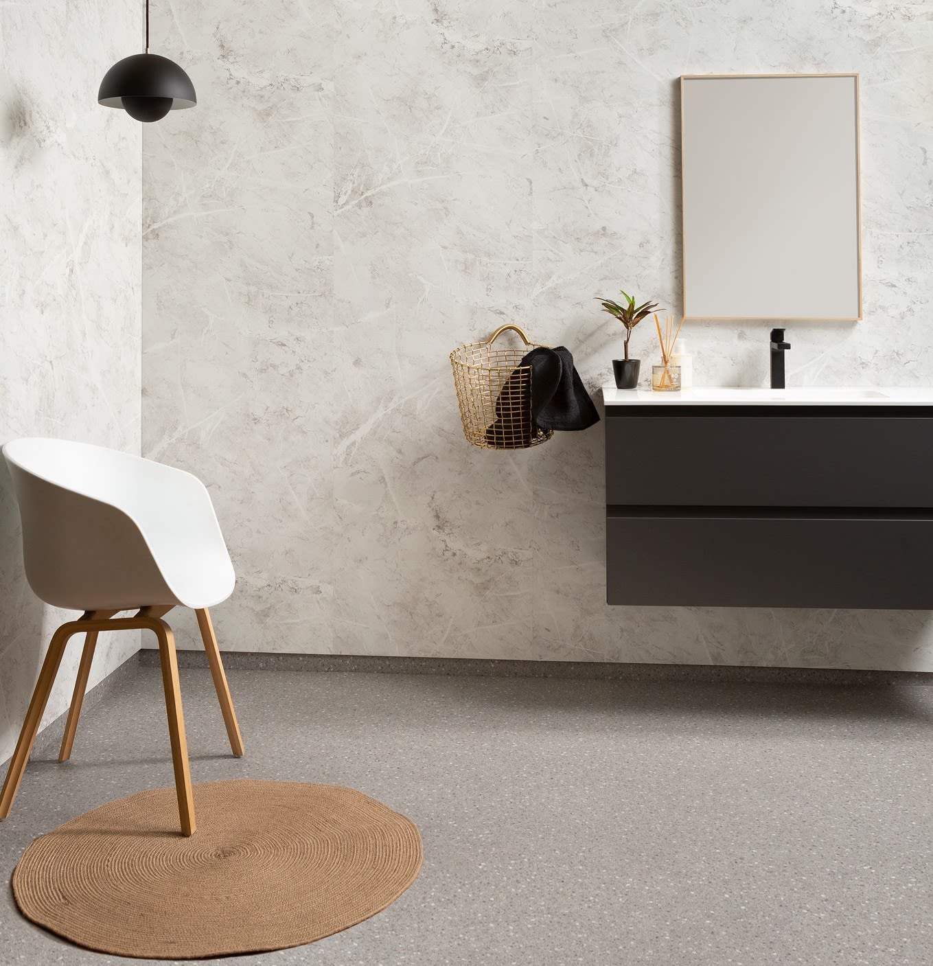 Minimalistisk baderom med hvit stol, rund brun matte, svart servant, gullkurv og grønn plante.