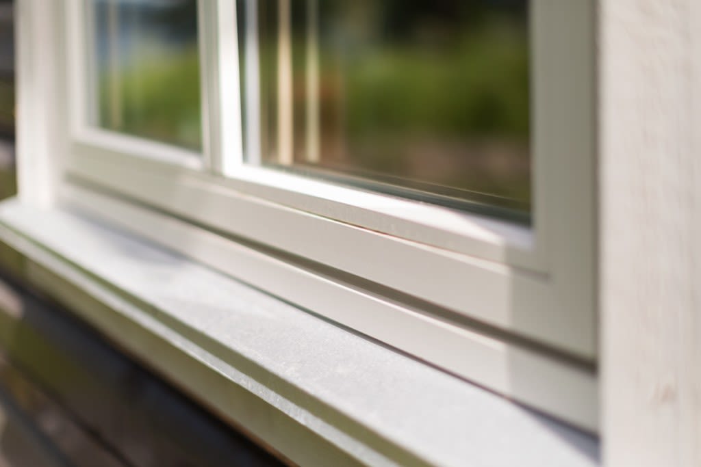 Nærbilde av hvit vindusramme og -karm med uskarp grønn hage i bakgrunnen
