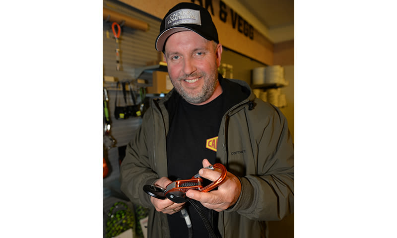 Person i mørk jakke og caps holder oransje karabiner i sportsutstyrbutikk.