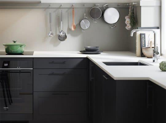 Moderne kjøkken: svarte skap, hvit benkeplate med oppvaskkum, hengende gryter og grønn kjele.