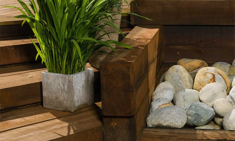 Ute: grønn plante i grå betongkrukke på brun treterrasse ved lyse dekorsteiner.