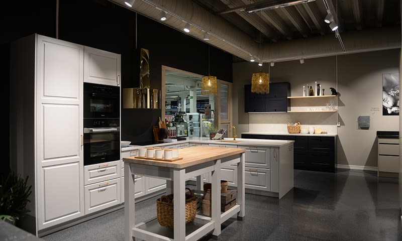 Moderne kjøkken i showroom med hvite og svarte skap, trespiseøy og gullpendler