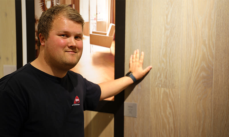 Person i mørk t-skjorte med BM-logo berører lys eikedør i interiørshowroom.