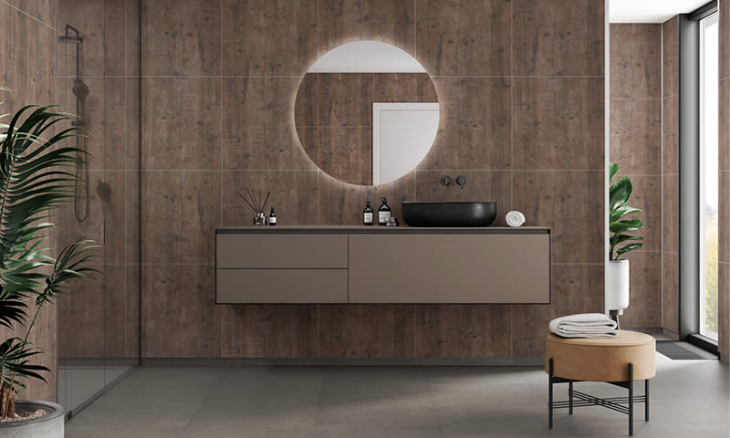 Moderne bad med brune fliser rundt bakbelyst speil, flytende møbel, svart vask, glassdusj og planter