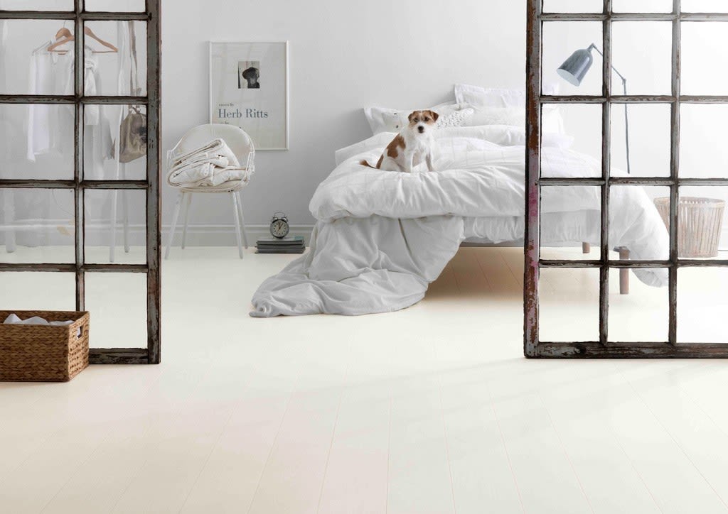 Lyst, hvitt soverom delt av rustikke glassdører, liten brun-hvit hund på sengen.