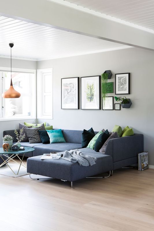 Lys stue med grå hjørnesofa, grønne og turkise puter, kobberpendel og planter