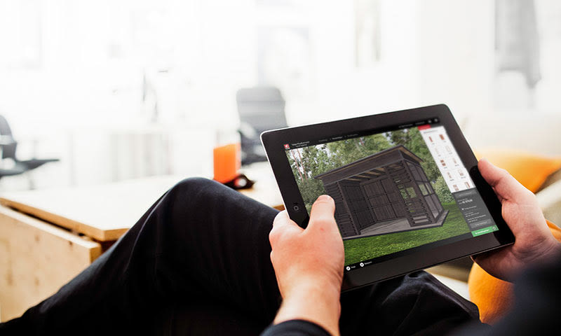 Person holder nettbrett som viser sort 3D-hageskur på grønt gress i lyst kontor.