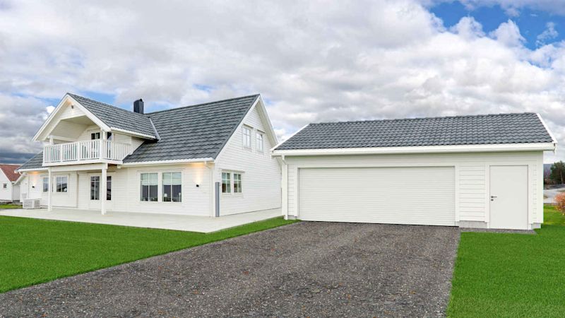 Hvit enebolig med grått tak og balkong, dobbelgarasje, grønn plen og overskyet himmel.