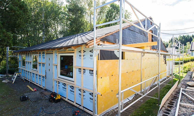 En enetasjes hus under oppussing med stillas, blå dampsperre og gule isolasjonsplater