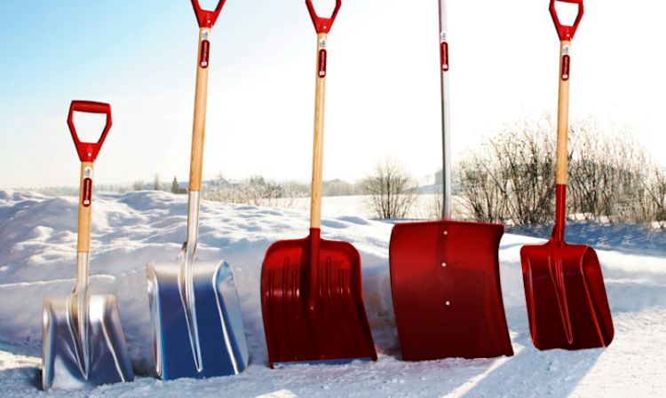 Fem snøspader med røde håndtak, to i aluminium og tre røde, plassert i snø mot vinterhimmel.