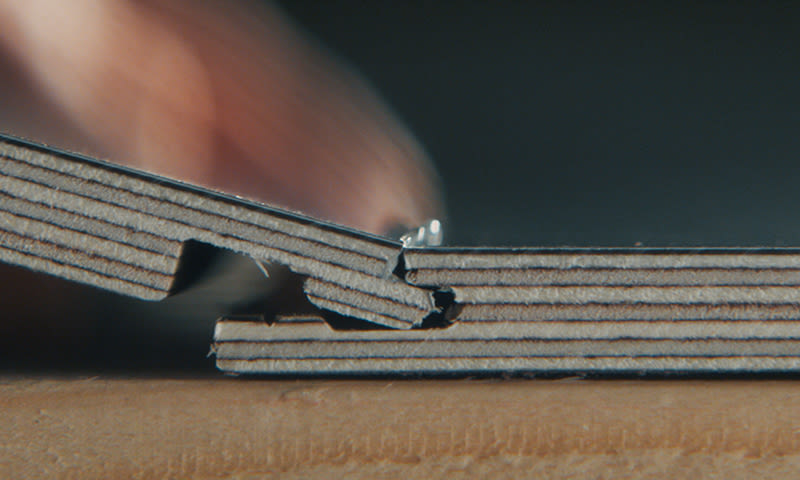 Nærbilde av lagdelt brun papp som bøyes ved hengsel, finger mot mørk bakgrunn