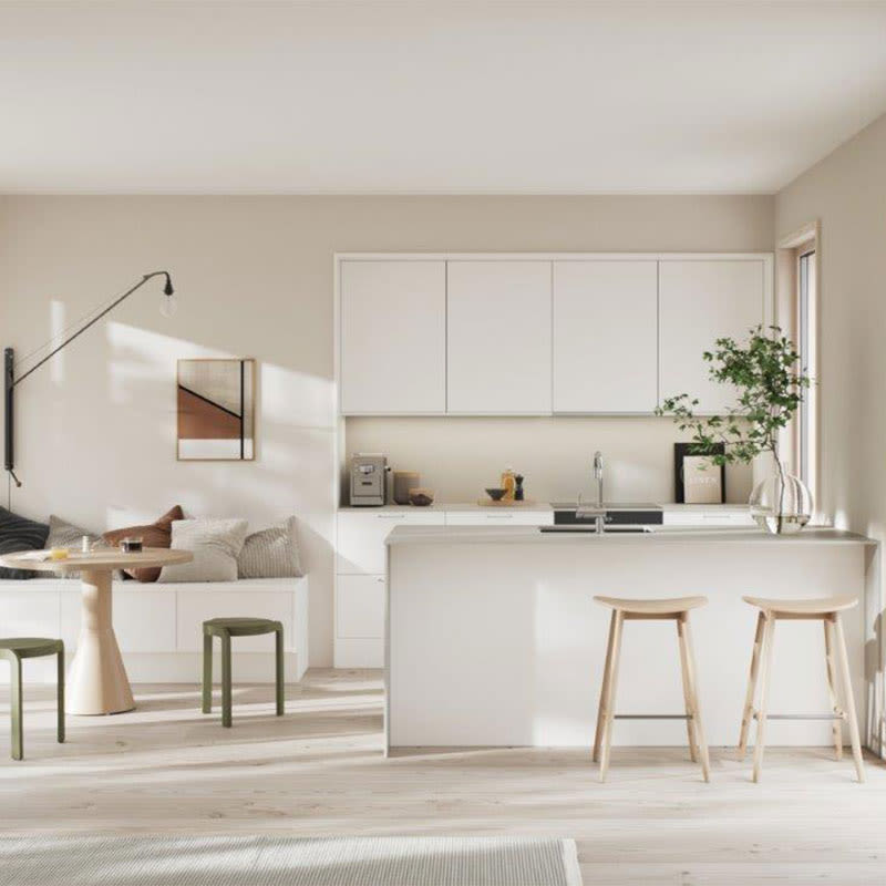 Åpent lyst rom med hvit kjøkkenøy, to trebarkrakker, rundt bord med grønne krakker, sofa, plante