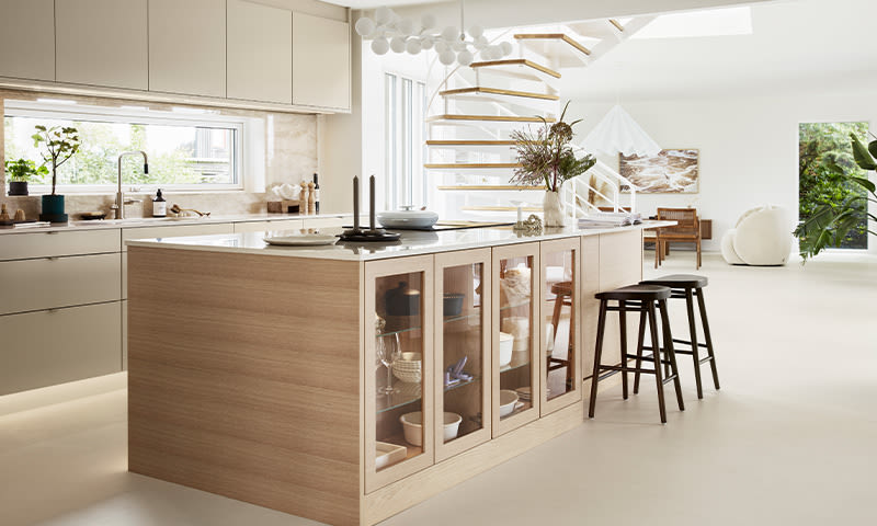 Lyst kjøkken med eikeøy og glassdører, tre svarte barkrakker og hvit spiraltrapp