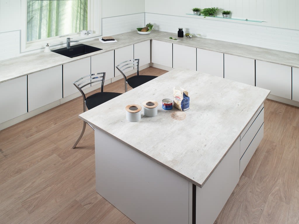 Lyst hvitt kjøkken med betonglook benkeplate og øy, to metallstoler og grønne planter