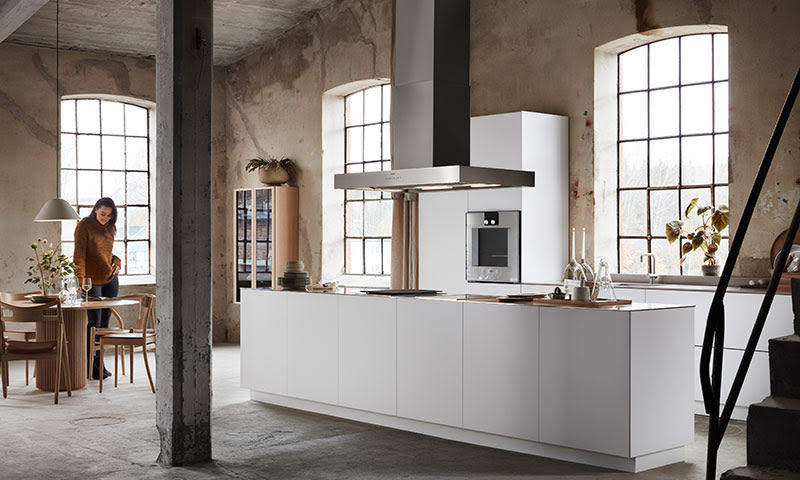 Lyst loftkjøkken i industristil med hvit øy, rå betongvegger og store vinduer.