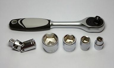 Krommetall skralle med svart-grått grep, fem pipenøkler og leddadapter på grå bakgrunn.