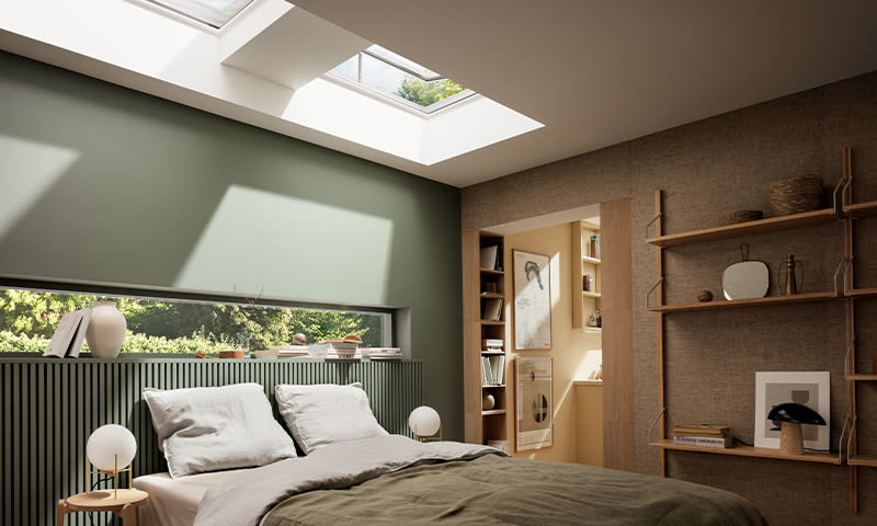 Skandinavisk soverom med grønne vegger, beige seng, takvinduer og treshylle med bøker.