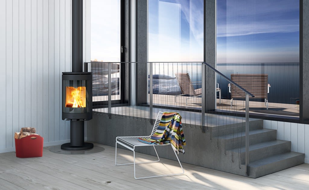 Moderne rom med svart vedovn, flammer, rød vedkurv, stol med farget pledd og havutsikt