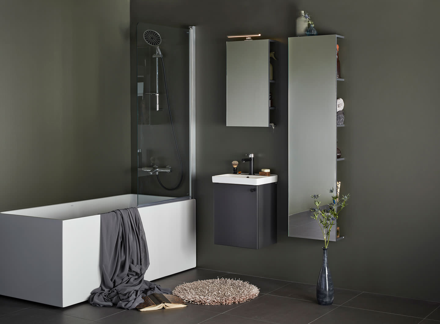 Moderne bad med mørkgrå vegger, hvitt badekar, dusj, svart servantskap, speil, høyt skap og vase