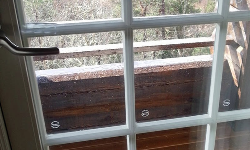 Regnvåte dråper på hvit vindusrute med utsikt mot mørk trekledning på balkong