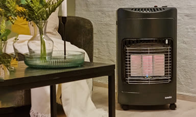 Sort gassovn med rødt varmeelement ved sofa og salongbord med gule blomster.