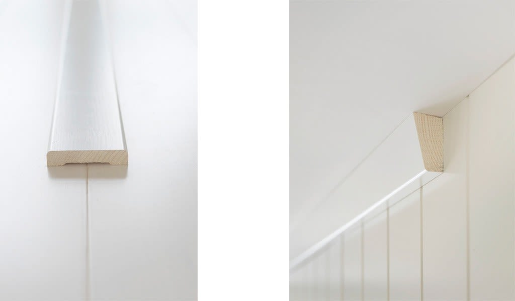 Nærbilde av hvite, vertikale trepaneler med list og ubehandlet trekonsoll under skråtak