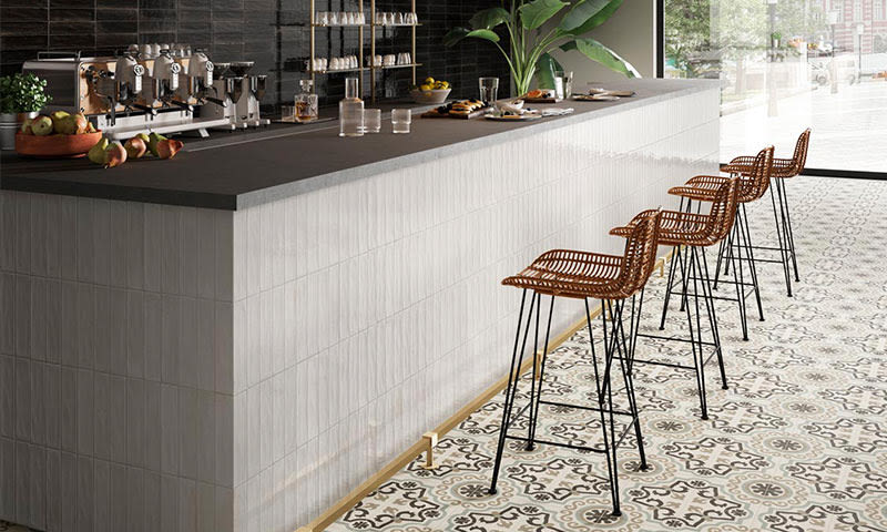 Moderne caféinteriør: hvit disk med svart benk, brune fletthøystoler, mønstret gulv.