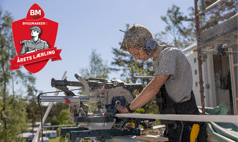 Lærling i verneutstyr sager hvit list med kap-/gjæringssag på solfylt byggeplass.