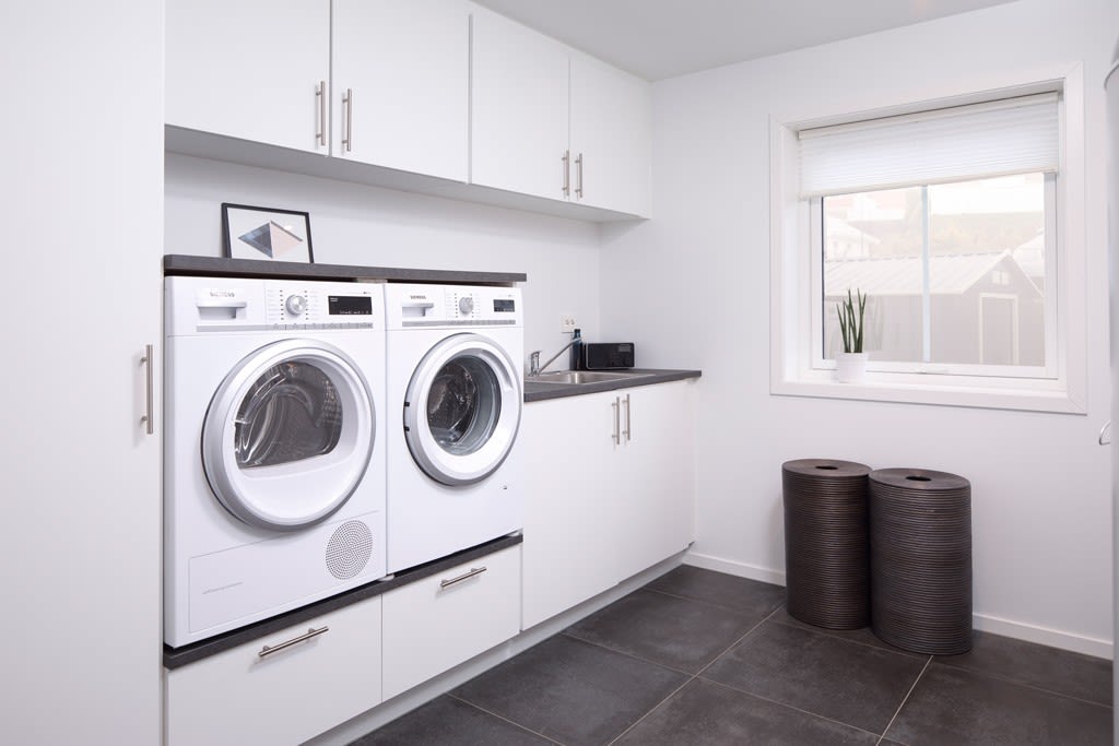 Lyst, moderne vaskerom med hvite skap, vaskemaskin, tørketrommel, vask og to mørke kurver