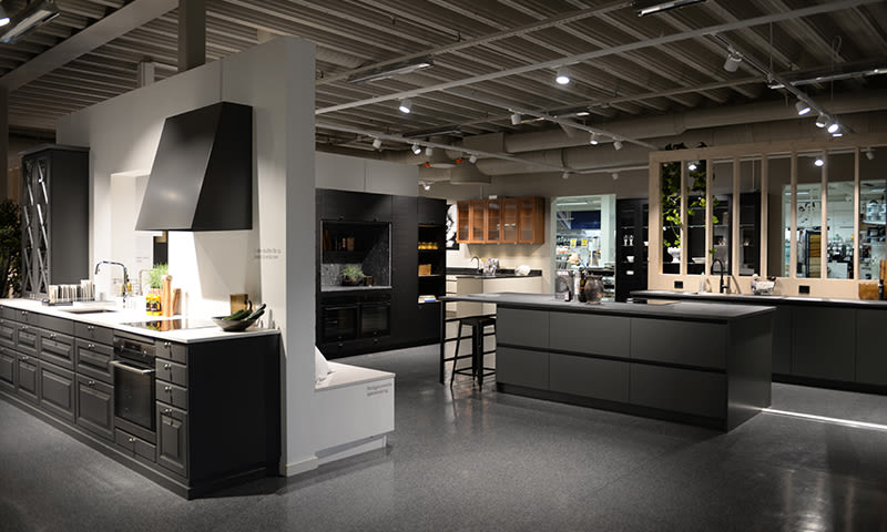 Moderne kjøkkenshowroom med svarte og hvite kjøkkenøy, barstol og blankt grått gulv
