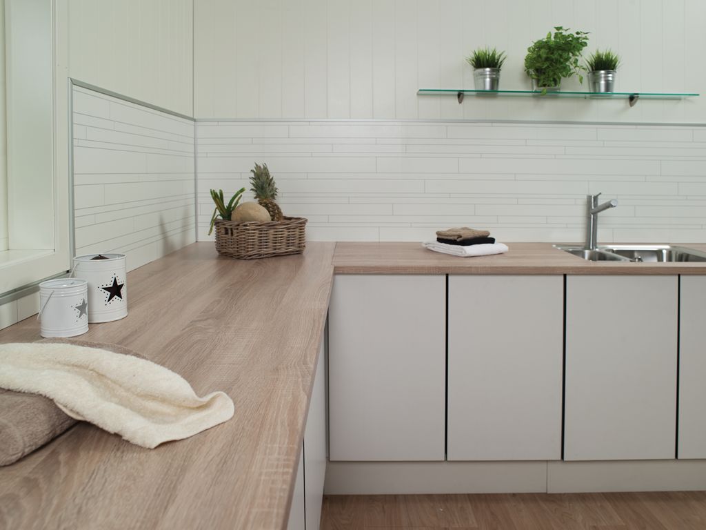 Moderne kjøkkenbenk med treplate, lysegrå skap, kurv med ananas og frukt, håndklær, planter